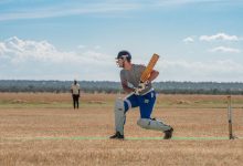 Cricketer prepares to bat on a bright sunny day in the field, displaying focus and concentration.