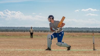 Cricketer prepares to bat on a bright sunny day in the field, displaying focus and concentration.