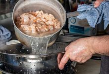 Professional chef draining boiled shrimps in a kitchen setting, captured mid-action.