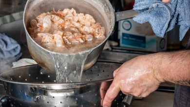 Professional chef draining boiled shrimps in a kitchen setting, captured mid-action.