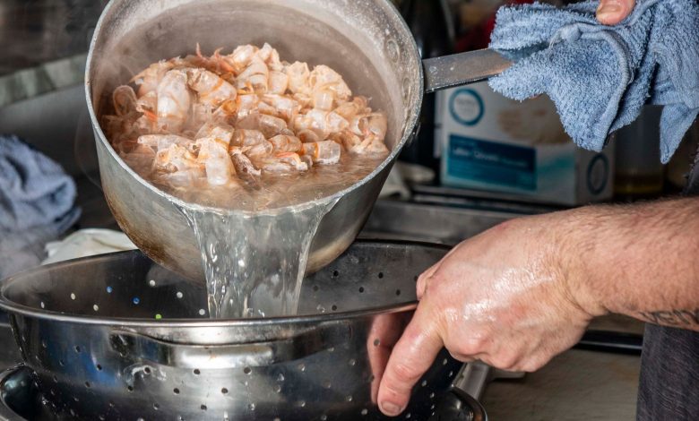 Professional chef draining boiled shrimps in a kitchen setting, captured mid-action.