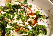 Close-up of a flavorful dahi vada garnished with fresh cilantro and spices in a white bowl.
