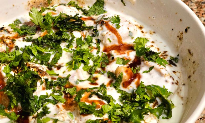 Close-up of a flavorful dahi vada garnished with fresh cilantro and spices in a white bowl.