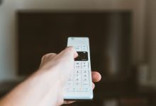 Close-up of a hand using a remote control to operate a television indoors.