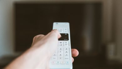 Close-up of a hand using a remote control to operate a television indoors.