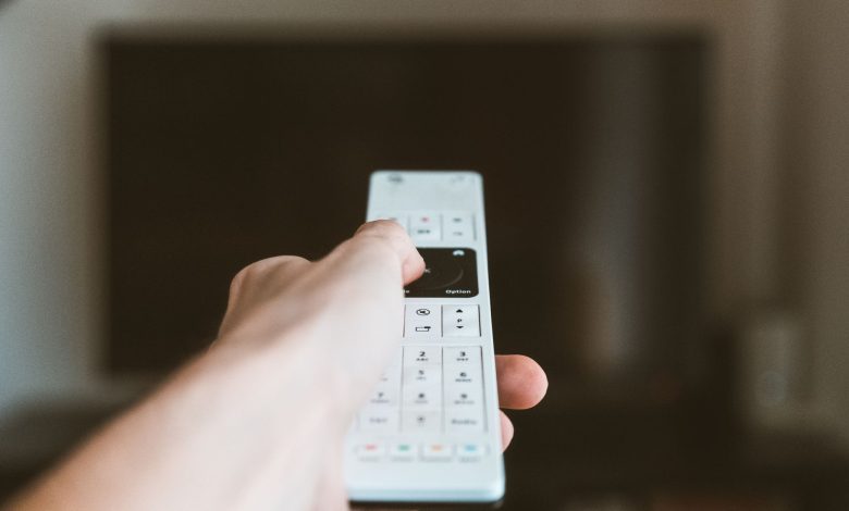 Close-up of a hand using a remote control to operate a television indoors.