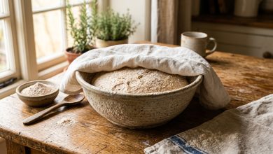 Bread and roti dough proofing inside a ceramic bowl under a cloth on a rustic kitchen table